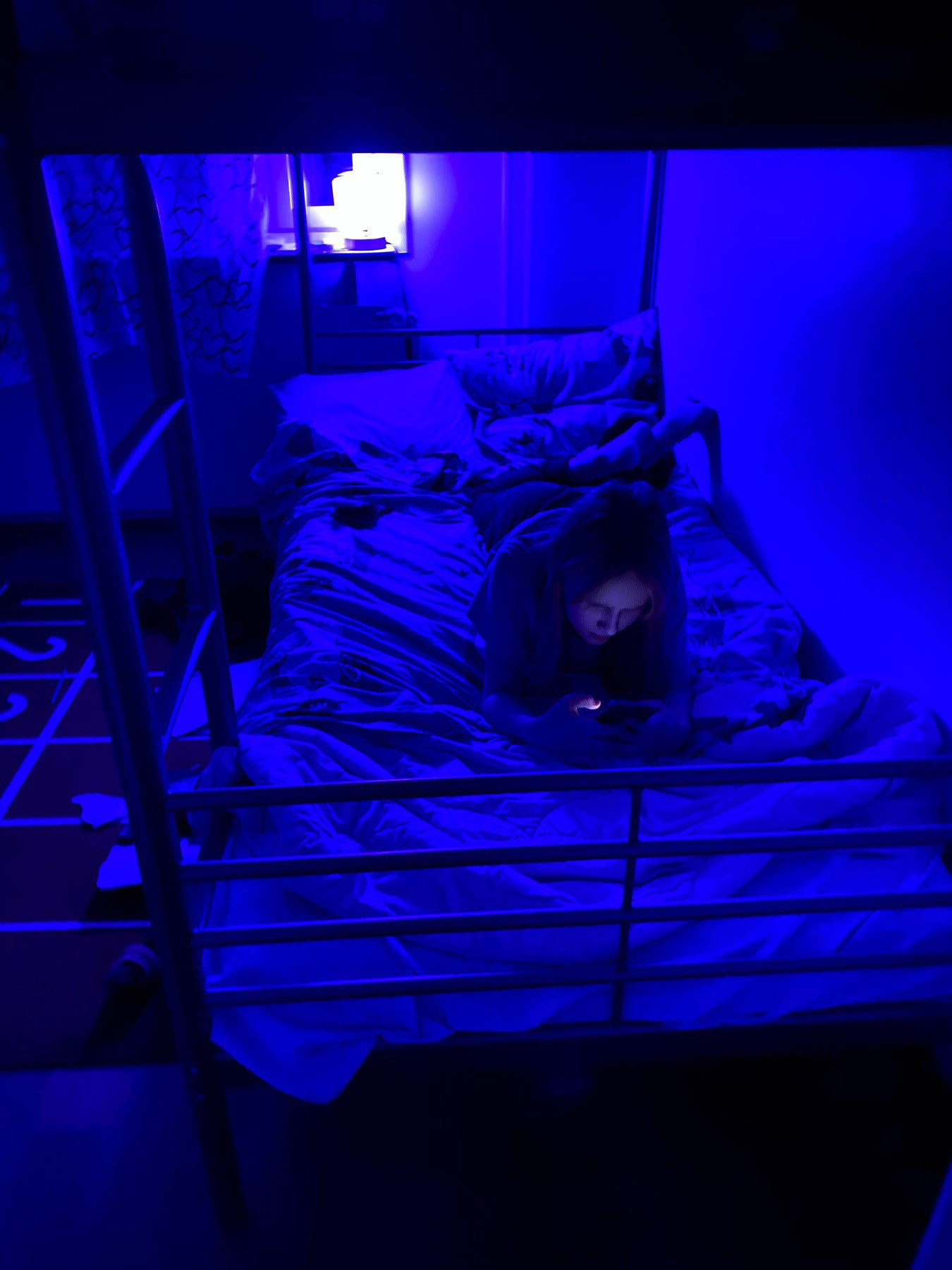 Blue lit room, bunk bed, a child on her phone