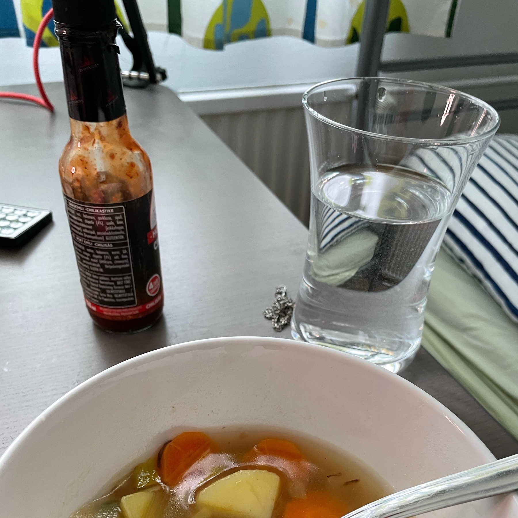 lentil soup in a bowl, hot sauce bottle, big glass of water on a computer desk