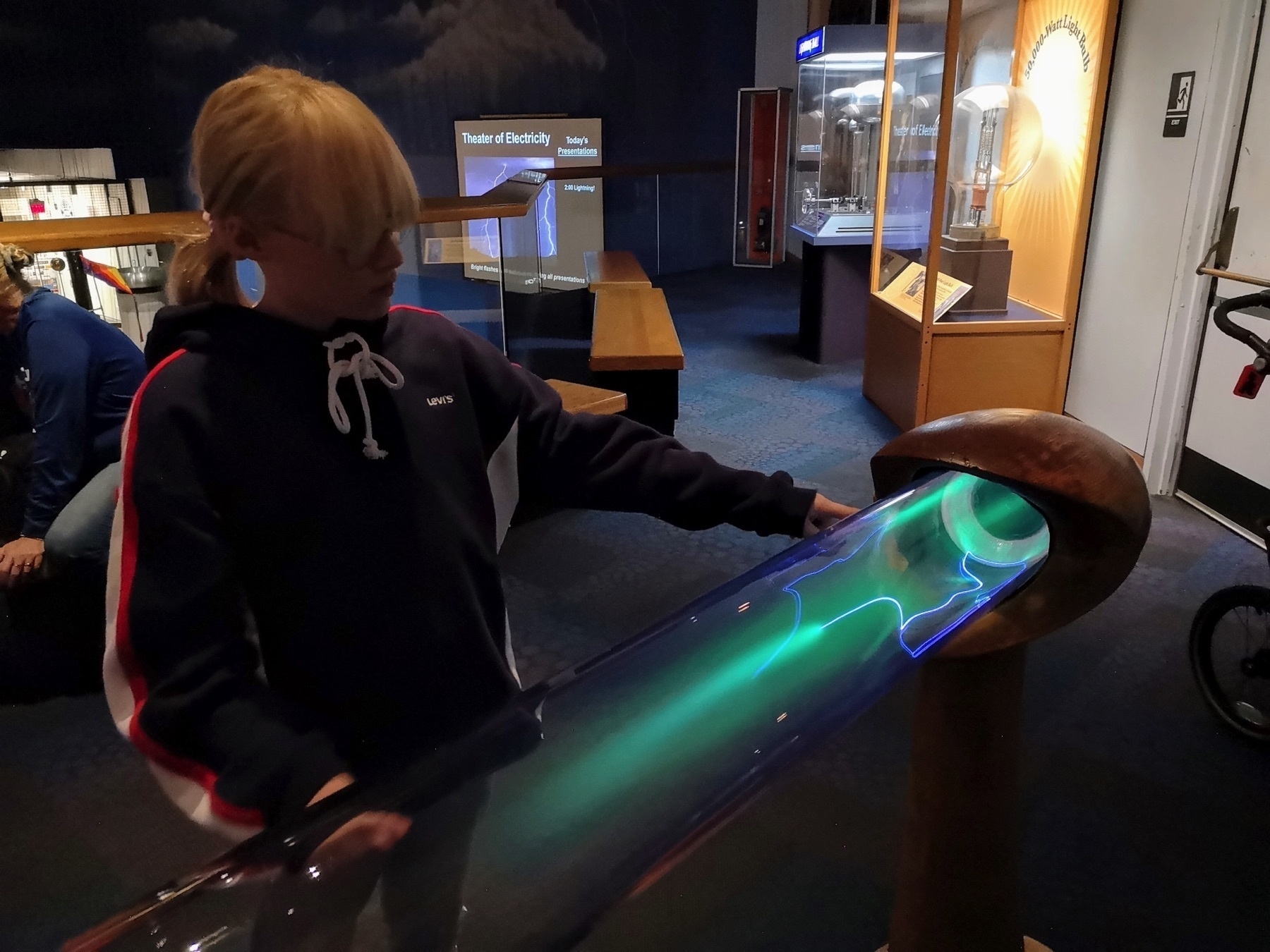 plasma tube, teenager touching it, “theater of electricity” signs on the background